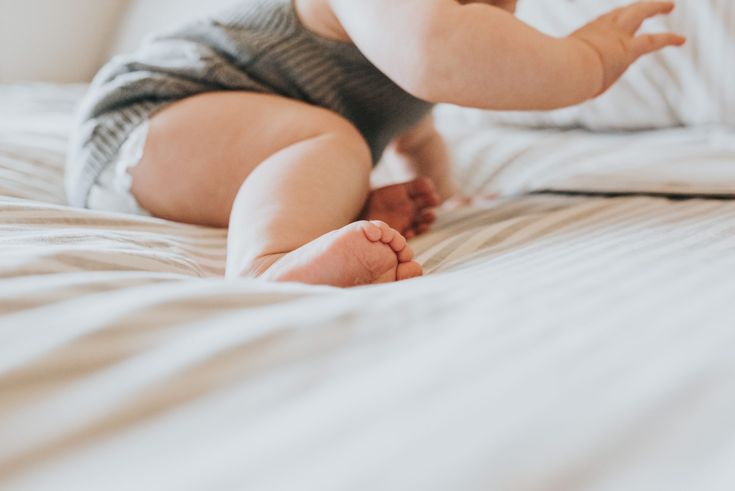 a young baby crawling on a bed, just the bottom half of the baby's body is visible