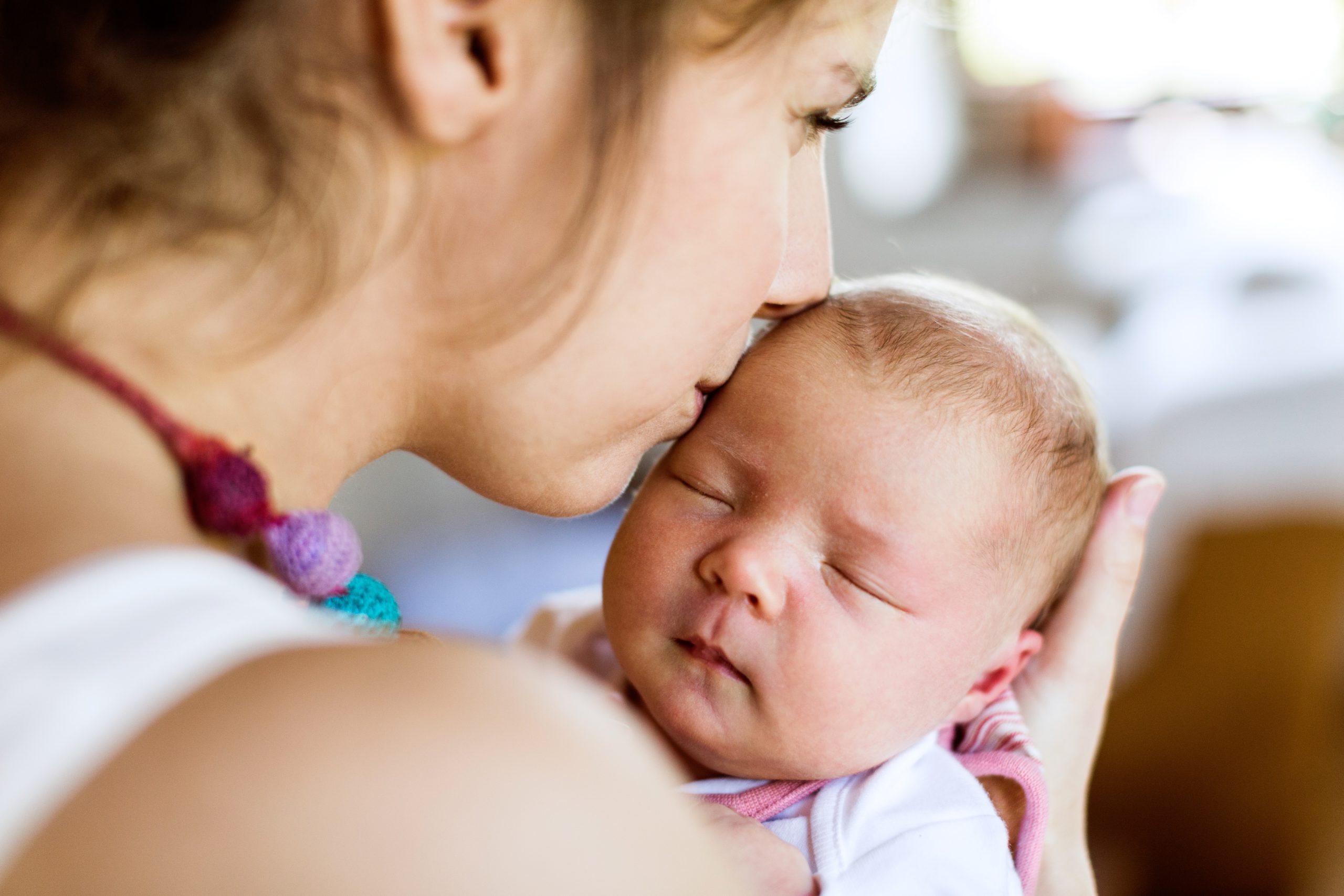 A mother lovingly kisses the top of her sleeping newborn's head.