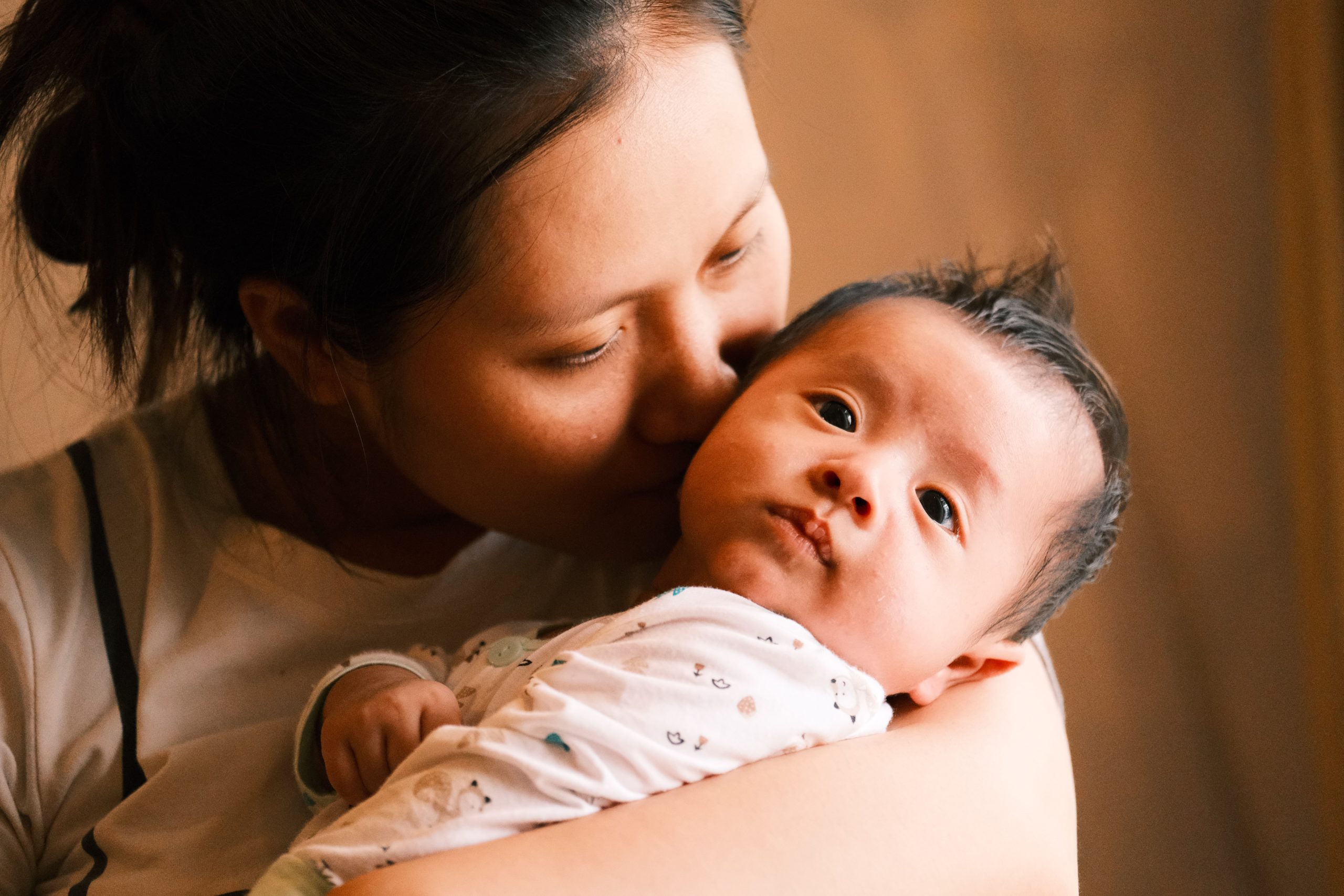 A mother cradling her newborn baby and nuzzling his cheek.