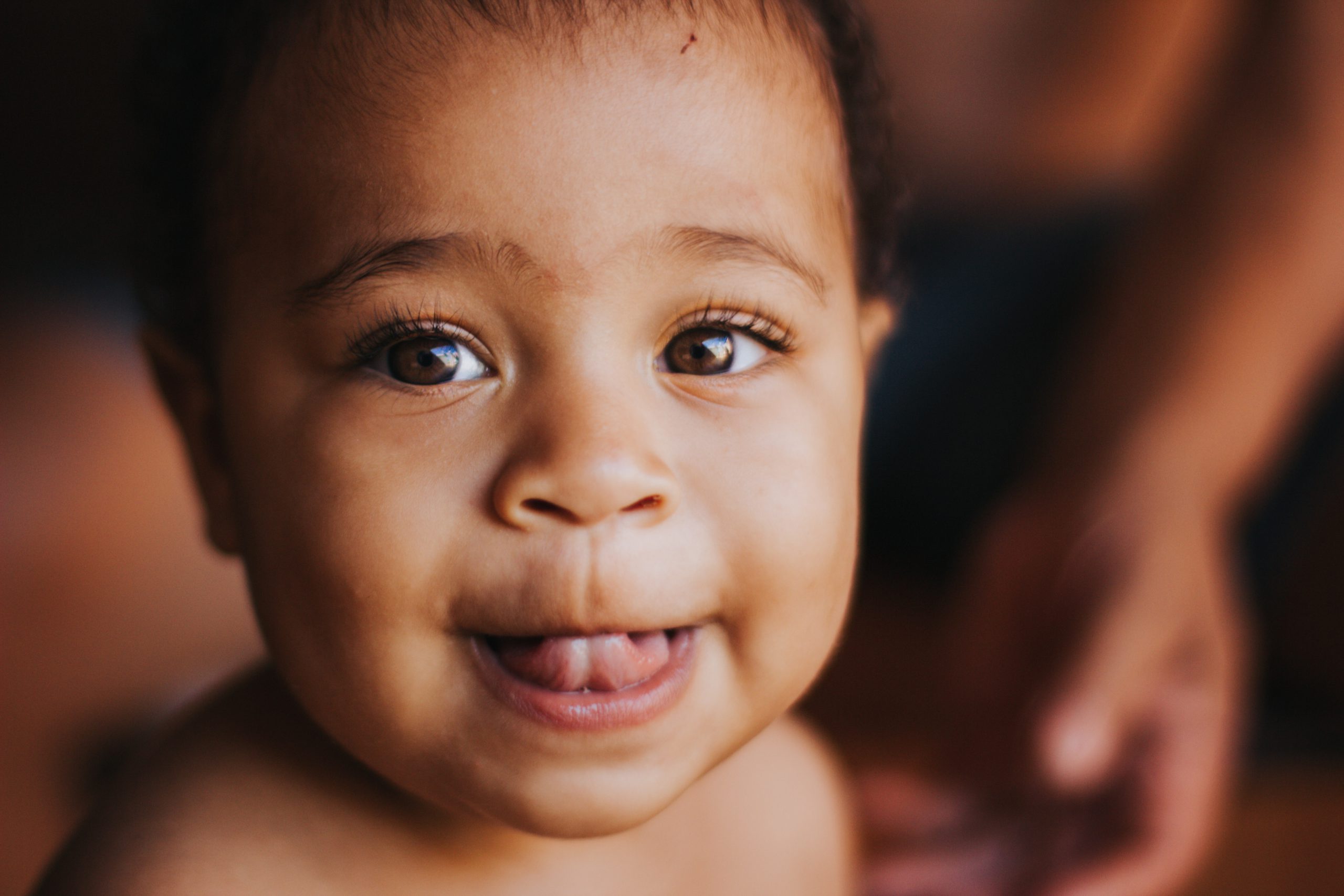 A toddler looks straight at the camera, with his tongue out and a twinkle in his eyes.