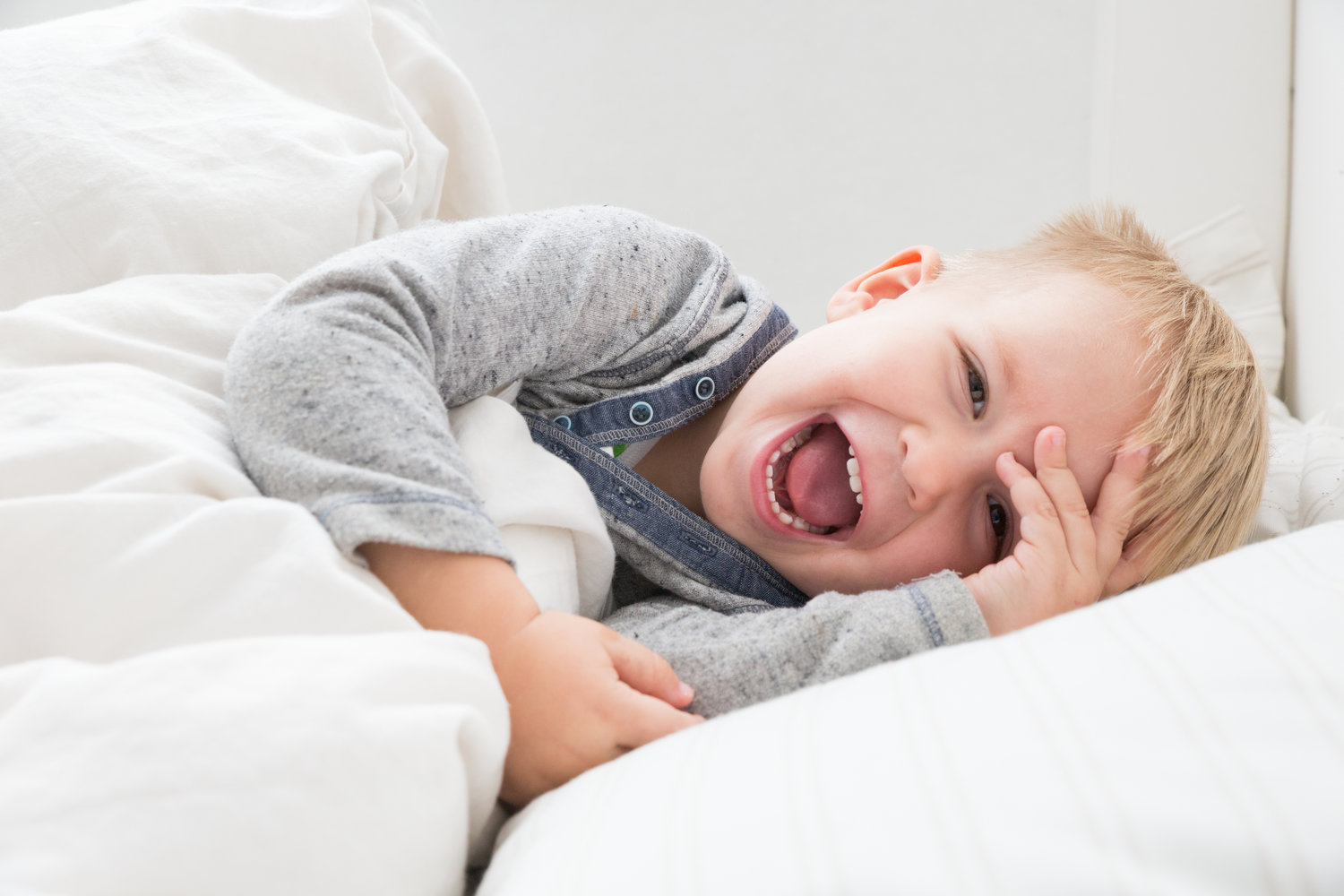 A laughing toddler laying down in bed